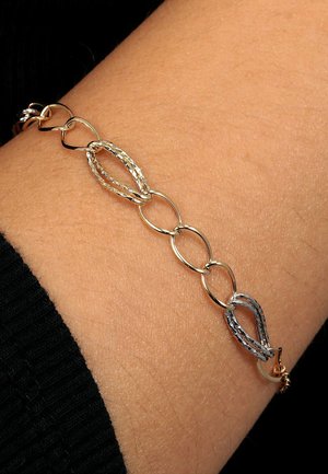 Armbanduhr aus Gold und Silber mit ovalen und gedrehten Gliedern, die eine Kombination aus glatten und strukturierten Oberflächen zeigt, die an der Haut zur Geltung kommen.