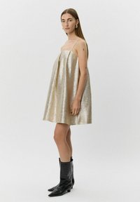 Metallisk guld mini-klänning med spagettiband, plisserad design och en slät yta. Matchas med svarta ankelfärgade stövlar i krokodilmönster.