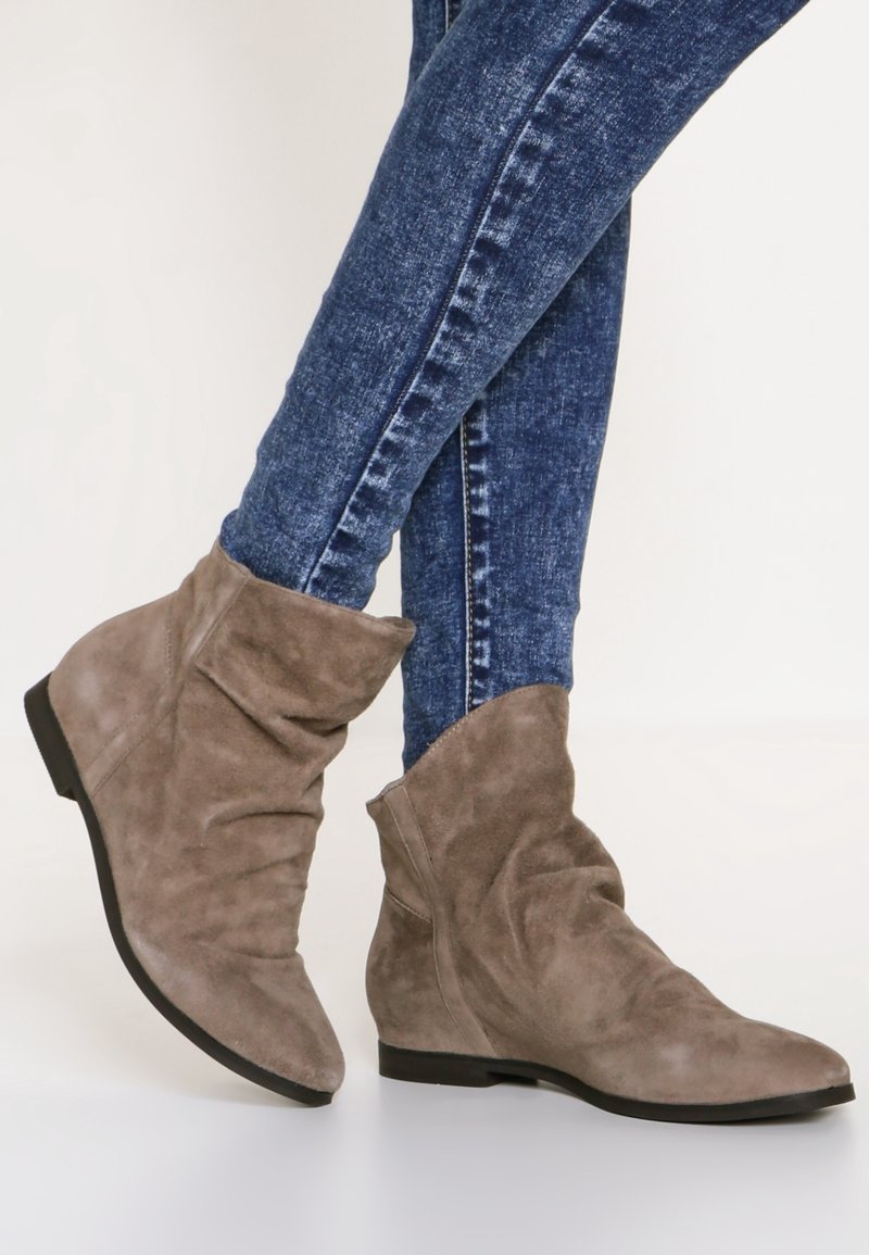 Bottes marron en suède décontractées portées avec un jean skinny bleu, vues de côté et de face en léger angle sur fond clair.