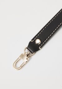 Bracelet en cuir noir avec des coutures blanches, doté d'un fermoir en métal doré et d'un détail à bouton pression à une extrémité.