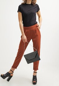 Camiseta negra de manga corta, pantalones ajustados color óxido y sandalias de plataforma negras. Los accesorios incluyen un bolso negro con tachuelas y una correa de cadena.