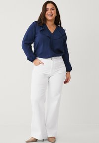 Blusa blu navy con colletto arricciato e maniche lunghe, abbinata a pantaloni bianchi a gamba larga e ballerine beige a punta. Texture morbida.