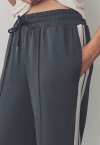 Laivastonsiniset urheiluhousut, joissa on joustava vyötärönauha ja kiristysnauha, sivutaskut sekä kontrastivalkoiset raidat sivuilla.