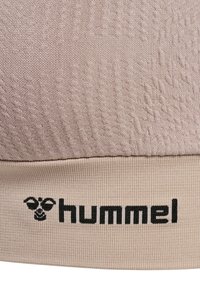 Close-up van beige textuurstof met geribde rand met zwarte hummel merknaam en logo.
