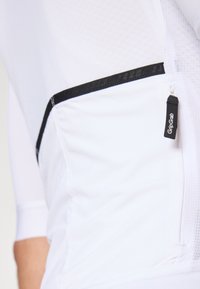 Hvit sykkeltrøye med strukturt stoff, svarte detaljer og en liten glidelåslomme merket "GripGrab." Har lange ermer og en tettsittende design.