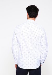 Weißes Langarmhemd mit dunkelblauem Punktemuster, klassischem Kragen und Knopfmanschetten. Glattes Material, taillierte Passform auf der Rückansicht.