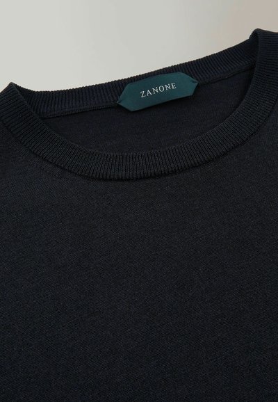 Pull en tricot noir avec un col rond côtelé et une petite étiquette verte portant le mot "ZANONE". Texture douce, design décontracté et forme classique.