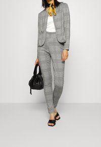 Grårutigt kostym med en figursydd blazer och avsmalnande byxor. Bärs med en vit topp, svart handväska och svarta sandaletter med öppen tå. Inkluderar en gul halsduk.