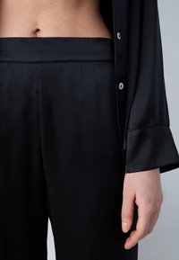 Zwarte satijnen loungewear set met een overhemd met knopen, een kraag en lange mouwen, gecombineerd met bijpassende broek.