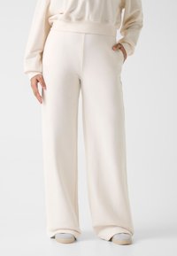 Kremowe, szerokie spodnie dresowe wykonane z miękkiego, teksturowanego materiału z bocznymi kieszeniami. Z subtelnym logo przy pasku.