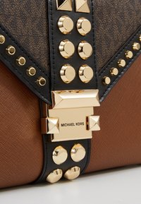 Sac à main marron texturé avec des anses noires ornées de clous dorés et un fermoir doré gravé Michael Kors.