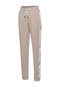 Beige Jogginghose mit elastischem Bund, Kordelzügen und weißen seitlichen Streifen mit schwarzem Text. Weicher Stoff, schmal zulaufendes Bein.