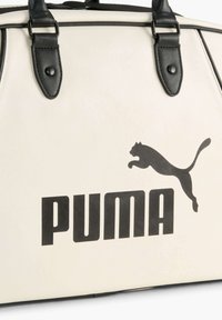 Valkoinen laukku mustilla yksityiskohdilla, jossa on iso musta "PUMA" -logo ja hyppivä puma -kuva. Sileä materiaali, rakenteellinen muoto, kaksinkertaiset kantokahvat.