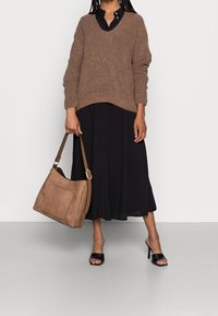 Maglione lavorato a maglia marrone, vestito nero con bottoni, mules nere con tacco e una borsa a spalla beige con pannello anteriore testurizzato e tracolla regolabile.