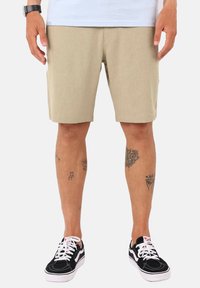 Shorts kaki avec une texture lisse, coupe droite, poches latérales, et baskets noires avec des lacets et des accents blancs.