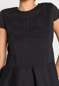 Vestido negro con escote redondo, mangas cortas, textura de rayas verticales y una falda acampanada con una cintura fruncida.