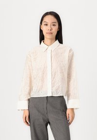 White embroidered blouse with floral lace texture, button-down front, and collar. Long sleeves with patterned cuffs. Cropped design.