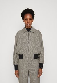 Grau karierte Bomberjacke mit einem frontalen Reißverschluss, schwarzen gerippten Bündchen und Saum. Glatte Textur und lockere Passform. Kombiniert mit passenden Hosen.