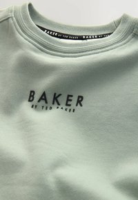Jasnozielona bluza z okrągłym dekoltem. Posiada na piersi wyraźne logo "BAKER by TED BAKER" w kolorze czarnym. Miękka tekstura materiału.