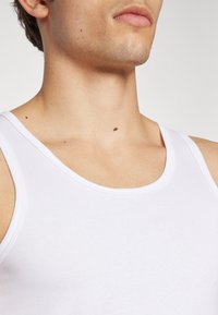 Débardeur en coton blanc avec un encolure arrondie et de larges bretelles, présentant une texture lisse et un design minimaliste.