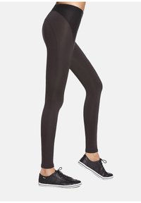 Czarne legginsy z wysokim stanem wykonane z elastycznego materiału, charakteryzujące się gładkim wykończeniem i dopasowanym krojem, zestawione z czarnymi trampkami.