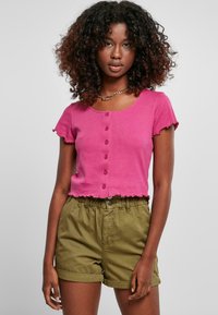 Fuksia kortermet t-skjorte med rund hals og dekorative knapper foran; sammen med olivengrønne shorts med elastisk liv.