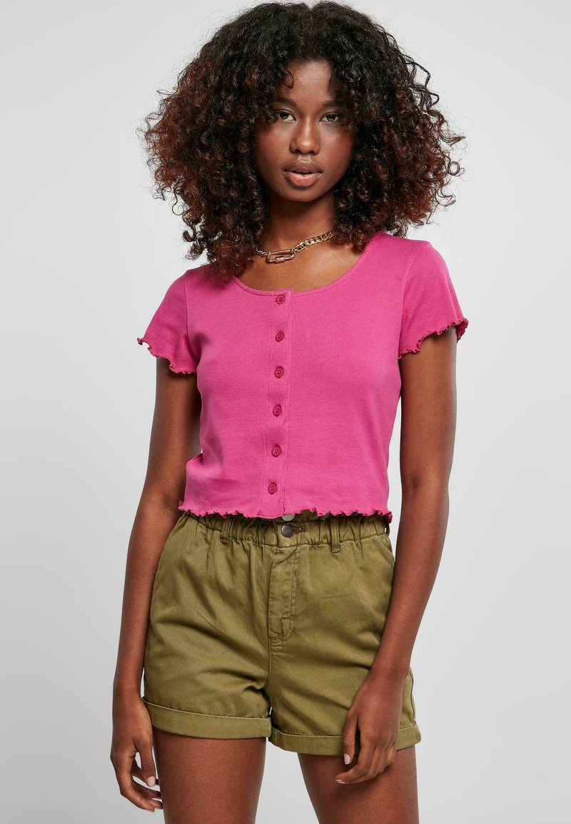 Fuksia kortermet t-skjorte med rund hals og dekorative knapper foran; sammen med olivengrønne shorts med elastisk liv.