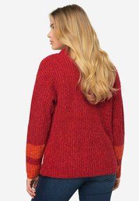 Roter Strickpullover mit langen Ärmeln, der ein strukturiertes Muster und orangefarbene Farbverläufe an den Bündchen aufweist. Lässige Passform und hoher Kragen.