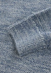 Pull en tricot présentant un motif texturé bleu et blanc. Les poignets sont retroussés, avec différentes nuances de bleu apportant de la profondeur au design.