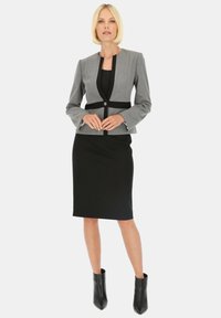 Szary strukturalny żakiet z czarnymi akcentami, w połączeniu z dopasowaną czarną spódnicą ołówkową i czarnymi botkami za kostkę, tworząc strzałkową sylwetkę.