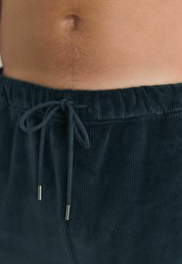 Tmavě zelené korduové šortky s elastickým pasem a šnůrkou, vybavené kovovými koncovkami, s jemným, texturovaným povrchem.