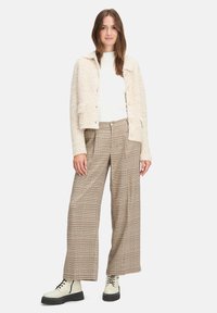 Veste texturée crème, top blanc, pantalon large à carreaux beige et marron, et bottes blanches à lacets épaisses avec une semelle noire épaisse.