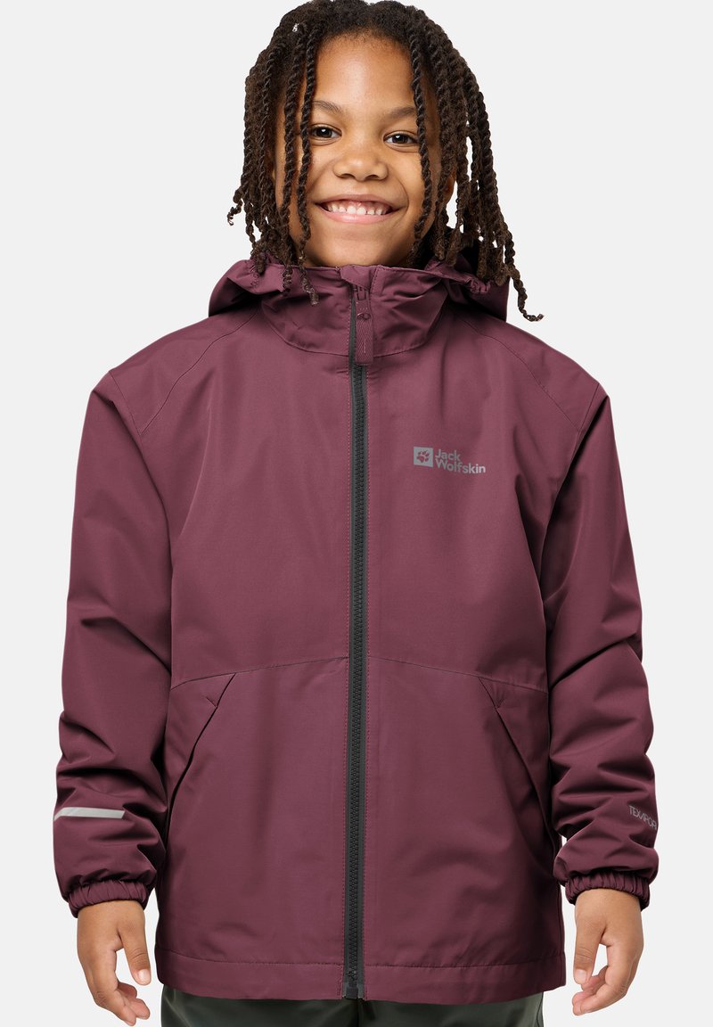 Smiling child with braided hair wearing a purple Jack Wolfskin hooded jacket with front zipper and elastic cuffs.