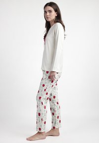Blusa blanca de manga larga con un acento rosa, combinada con pantalones de color claro que presentan un patrón impreso de objetos rojos y texto.