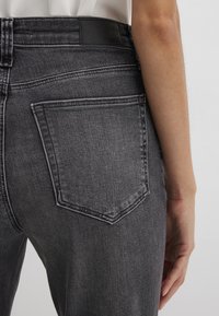 Faded black denim jeans with a high waist, featuring traditional back pockets, visible stitching, and a smooth texture.