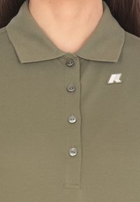Polo olive con tessuto testurizzato, dotato di tre bottoni, colletto a punta e un piccolo logo argento sul lato sinistro.