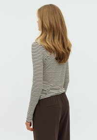 Striped long-sleeve top in cream and brown, fitted design. Worn with dark brown trousers featuring back pockets, viewed from the back.