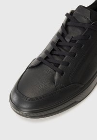 Black sneaker made of textured leather and mesh. Features flat laces, a rounded toe, and a rubber sole with a patterned tread.