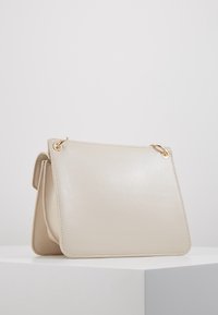 Beige läderhandväska med en slät textur, fyrkantig design, rundade hörn och guldfärgad hårdvara på toppen.