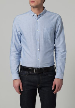 Lys blå, langermet skjorte med knapper og lomme. Stoffet har en subtil tekstur. Båret med mørke jeans og et svart belte.