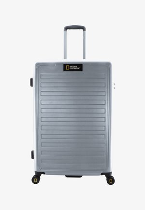 Silberner Hartschalenkoffer mit horizontalen Rillen, ausziehbarem Griff und vier schwarzen Rädern. Enthält ein National Geographic-Logo auf der Vorderseite.