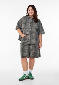 Ensemble en imprimé léopard composé d'un tissu léger, comprenant une chemise à col à manches courtes et un short assorti, associé à des baskets vertes.