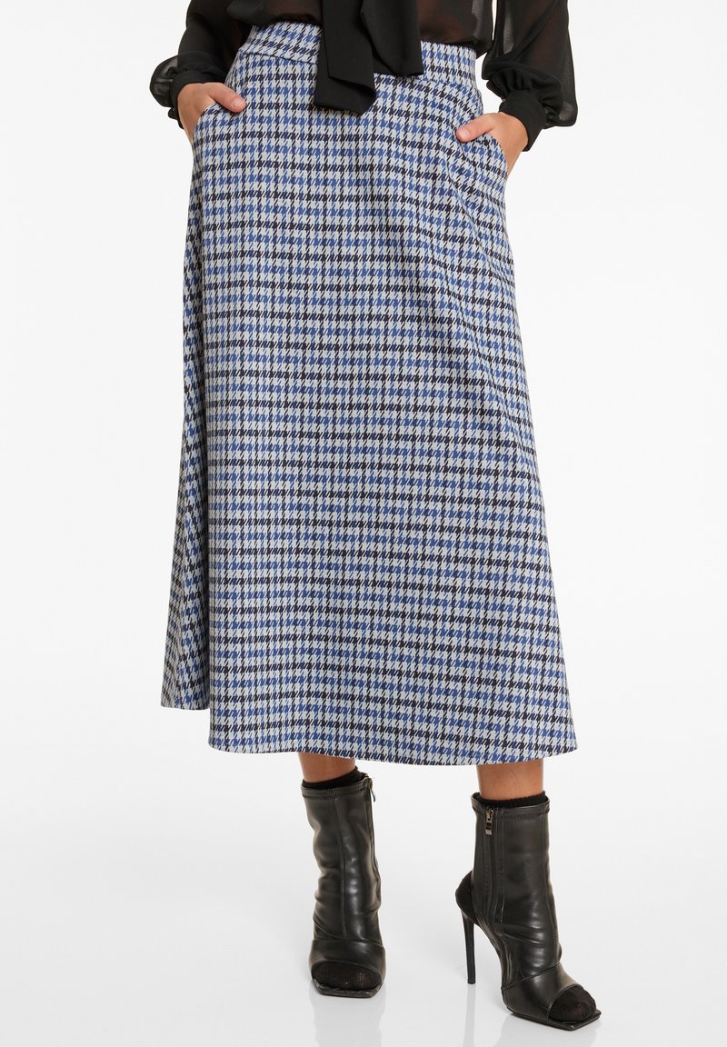 Midikleid in blau-weißer Hahnentwist-Musterung mit einem eng anliegenden Taillenbund und Taschen, kombiniert mit schwarzen Stiefeletten und einem transparenten schwarzen Oberteil.