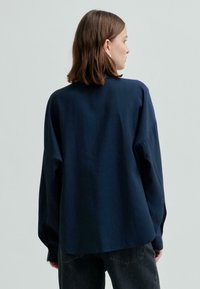 Laivastonsininen pitkähihaien paita, joka on valmistettu sileästä kankaasta, rentoa mitoitusta ja korkeaa kaula-aukkoa, yhdistetty tummaan farkkuihin.