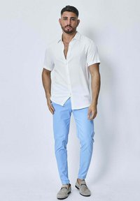Chemise blanche à manches courtes avec boutons, associée à un pantalon bleu clair et à des mocassins gris clair. Tissu lisse, coupe contemporaine.