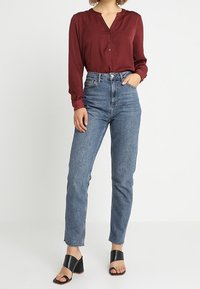 Blusa bordeaux con colletto a V, abbinata a jeans in denim blu a vita alta e sandali neri con tacco a blocco e punta aperta.