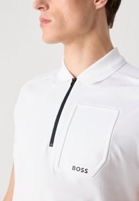 Biela polo tričko s zipsovým výstrihom, vybavené textúrovanou náprsnej vreckom a malým logom "BOSS". Priedušná tkanina s priliehavým strihom.