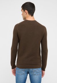Pull en tricot marron à manches longues, col rond et ourlet côtelé. Associé à un jean en denim bleu clair avec des détails de couture sur les poches arrière.