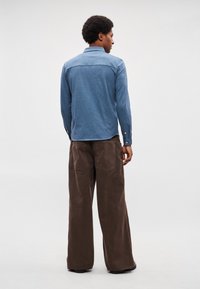 Camisa azul de mangas compridas com gola, combinada com calças castanhas de perna larga. A camisa apresenta uma textura suave, e as calças têm uma textura ligeiramente áspera.