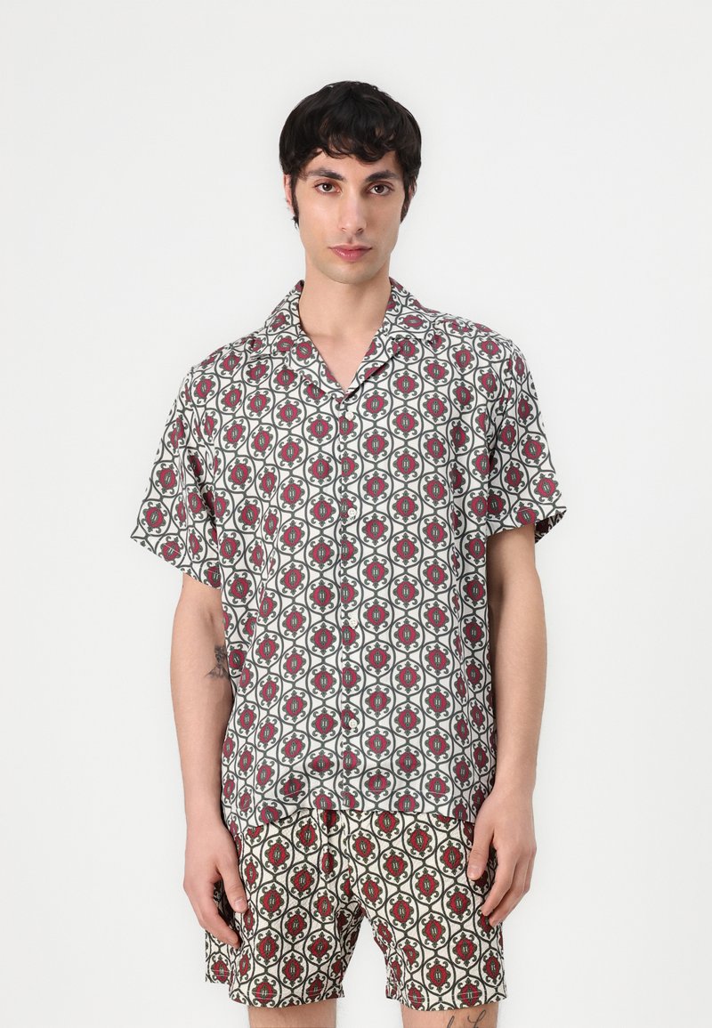 Kortærmet skjorte med knapper og matchende shorts i et let materiale, med et rødt og grønt geometrisk mønster på hvid baggrund.